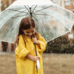 A happy girl hiding under umbrella from rain.