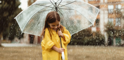 A happy girl hiding under umbrella from rain.