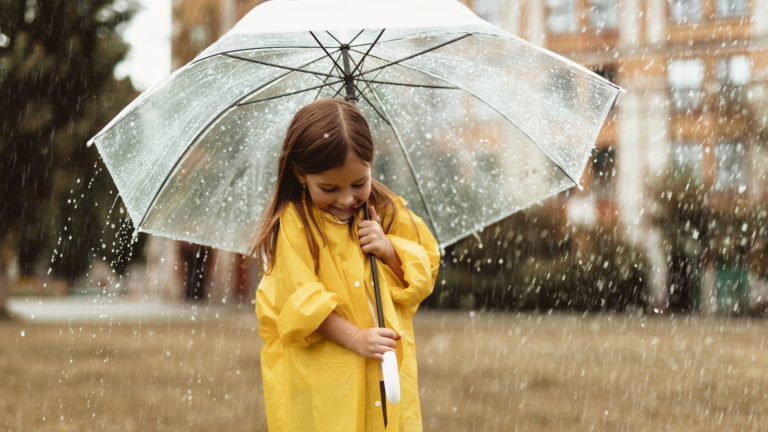 A happy girl hiding under umbrella from rain.