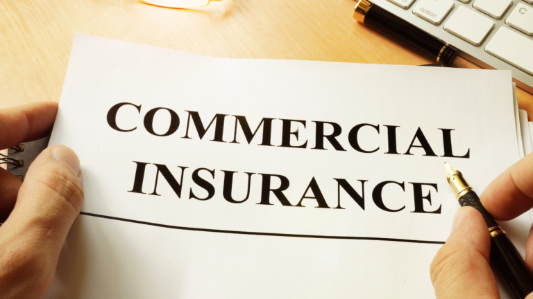 A hand holding a document with the words "Commercial Insurance" printed on it, accompanied by a pen and a keyboard on a desk.